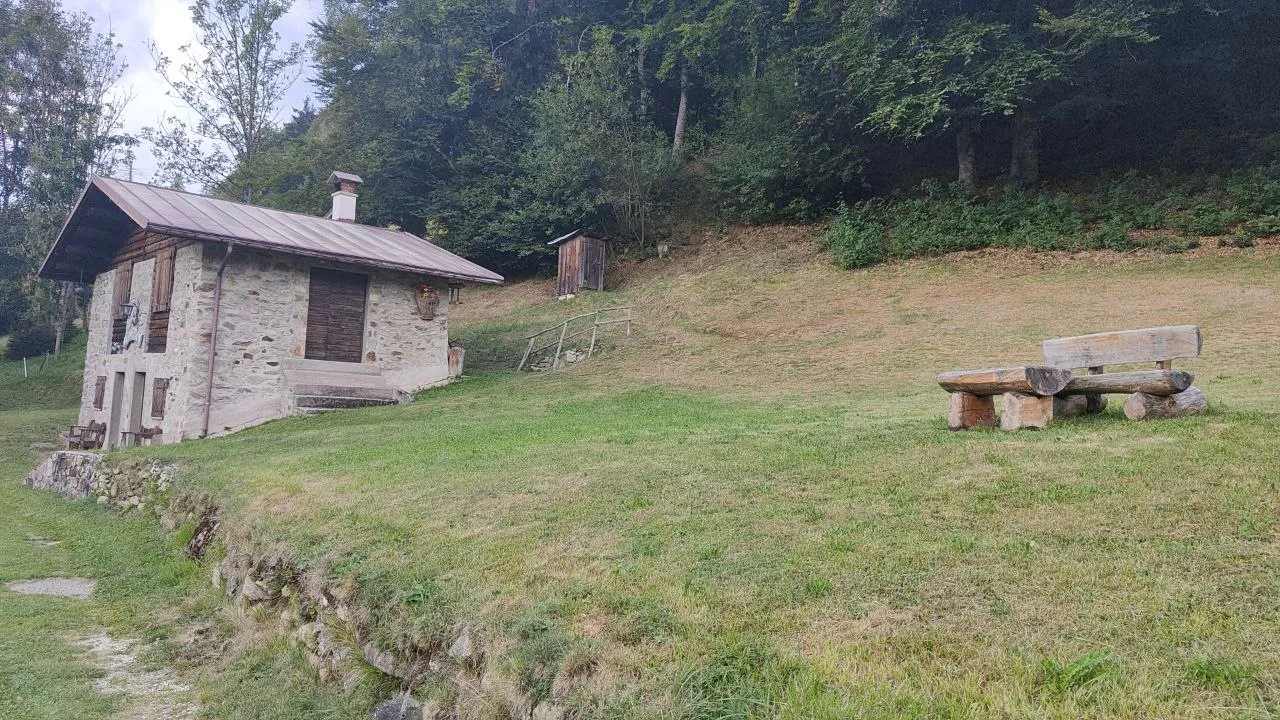 Baita secolare in pietra e legno con panche artigianali nel prato, lungo il sentiero verso Forcella Aurine